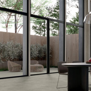 Ambiente moderno con pavimento Block Grey effetto cemento grigio chiaro, grandi vetrate con vista su giardino e arredi contemporanei in legno scuro