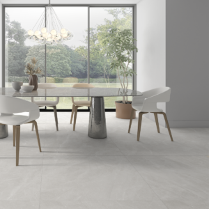 Sala da pranzo moderna con pavimento Isea Pearl effetto pietra grigio perla in formato 100x100, tavolo rotondo grigio con sedie bianche, lampadario di design e grande vetrata con vista su giardino