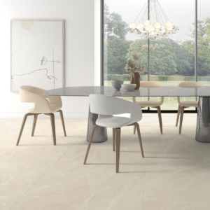 Sala da pranzo luminosa con pavimento Isea Sand effetto pietra sabbia beige in formato 100x100, tavolo rotondo bianco con sedie beige chiaro, lampadario moderno e grande vetrata con vista su giardino verde