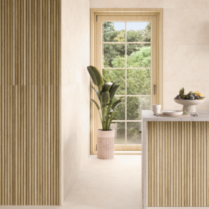 Ambiente luminoso con pavimento Finlandia Arce effetto legno acero chiaro in formato 60x120, pareti rivestite con listelli verticali in legno dorato, finestra con vista su giardino e piante decorative