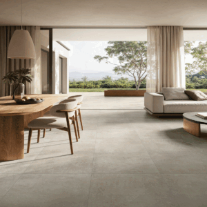 Soggiorno luminoso con vista sulla natura, pavimento Tex-Beige effetto cemento beige caldo, arredi in legno naturale e tende color crema