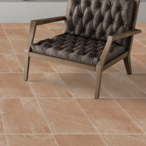 Salotto accogliente con pavimento Brenta Cotto Amb effetto cotto ambra in formato quadrato, poltrona vintage in pelle scura, parete neutra testurizzata e atmosfera calda rustico-contemporanea