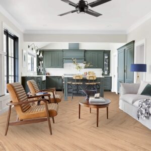 Open space moderno e luminoso con pavimento Valdivia Natural effetto legno naturale posa a spina di pesce, poltrone in pelle cognac, cucina con mobili verde petrolio, divano chiaro e ventilatore a soffitto in ambiente ampio e contemporaneo